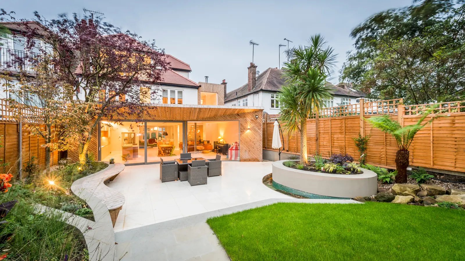 A finished patio and garden beside a lit house in the evening